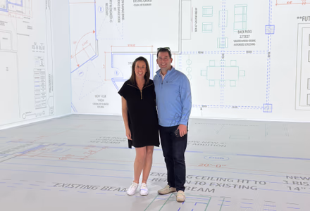 A couple standing inside a 1:1-scale floor plan projected on the Walk Your Plans NWA studio canvas